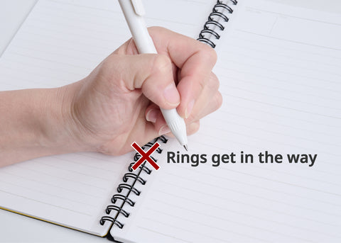 Left-handed person writing in planner, rings from spiral binding interfere with smooth writing, showing a common issue with traditional planners.