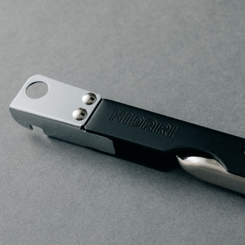 Versatile left-handed can opener with matte black finish, 3-in-1 functionality for cans, bottles, and hole punching, ergonomic design for left-handed users, made in Japan by HIDARI.