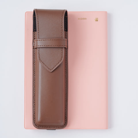Recycled leather book strap pencil case with adjustable elastic band, shown attached to a notebook.