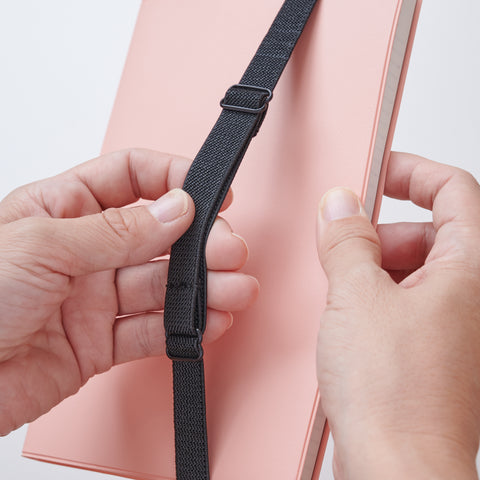 Recycled leather book strap pencil case with adjustable elastic band, shown attached to a notebook.