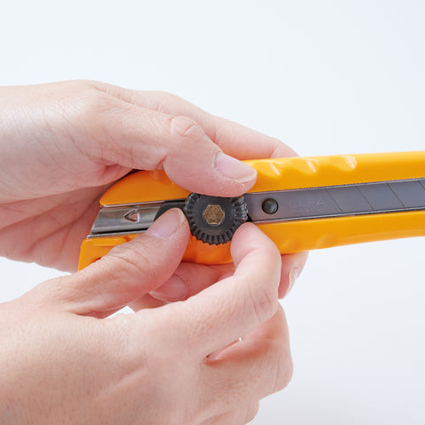 Left-handed OLFA utility knife with ergonomic design, reversed lever for smooth blade operation, includes two replacement blades, suitable for packaging, crafting, and DIY, made in Japan.