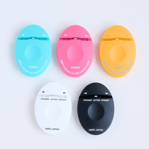 Five colorful ceramic letter openers in blue, pink, yellow, black, and white, showcasing a Japanese-made ambidextrous design for easy envelope opening.