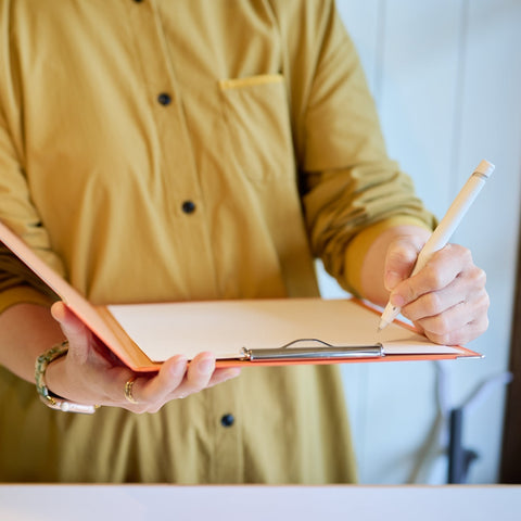 A user writing notes with a left-handed clipboard designed for left-hand use